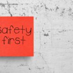 Red sticky note with the text “Safety First” on it posted to a wall with chipping paint.