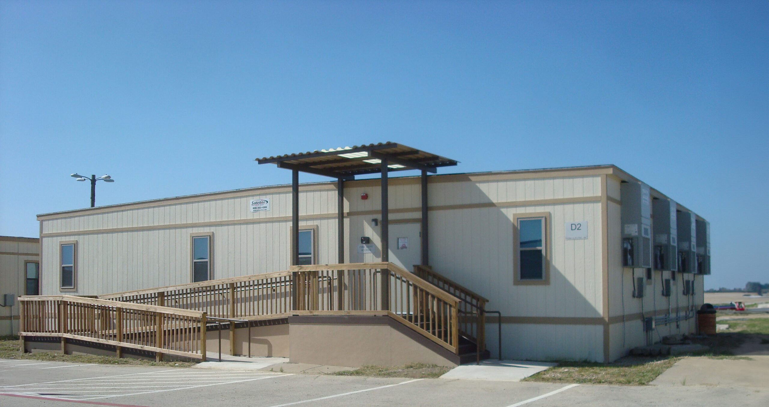 A beige modular building with a wooden ramp and stairs leading to the entrance.