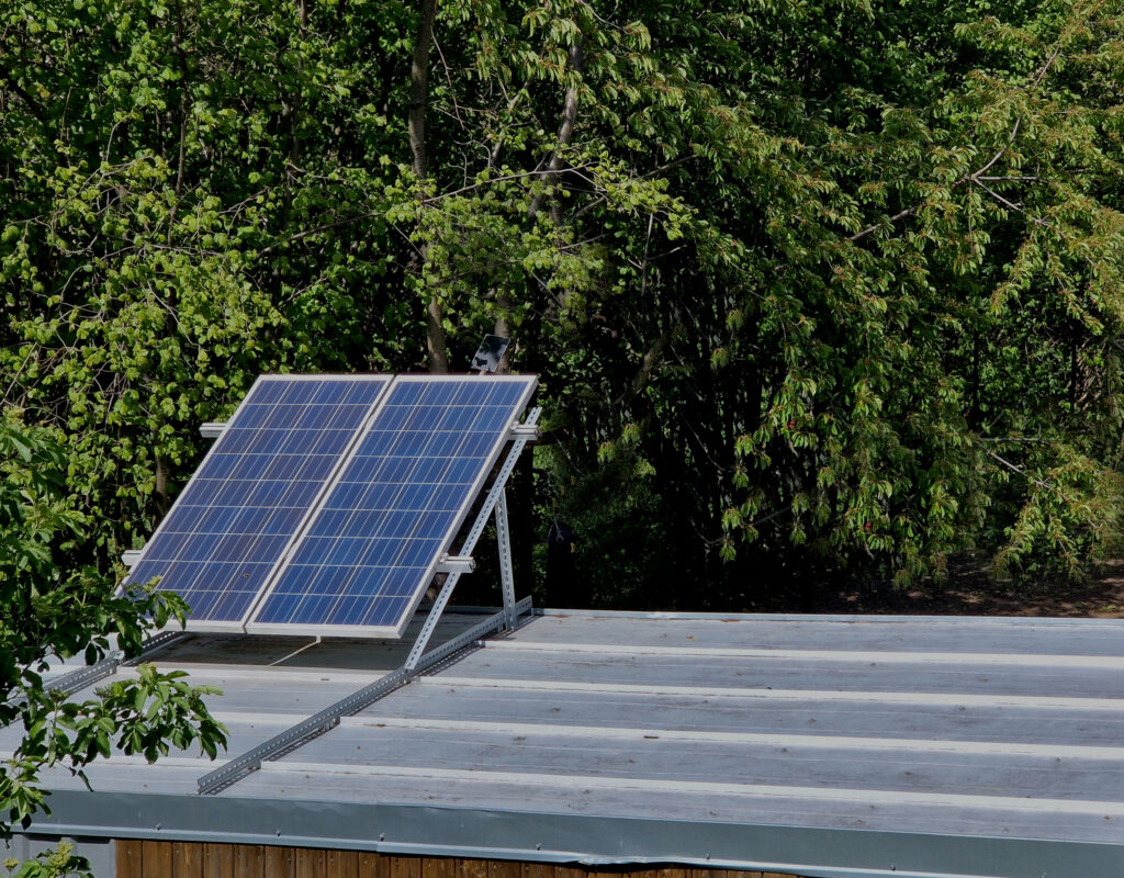 A solar panel installed on the roof of a modular building surrounded by trees.