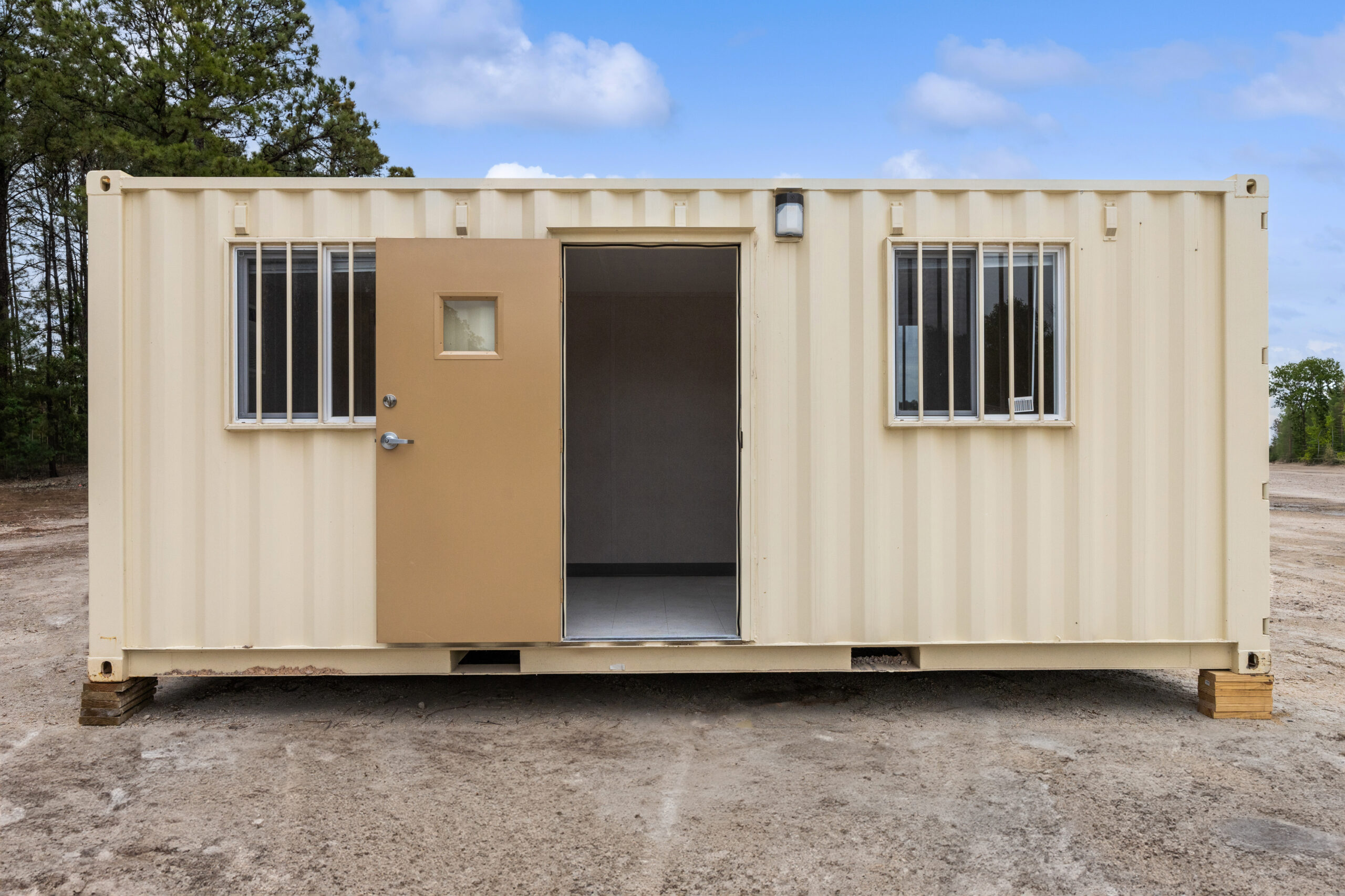 External view of a ground-level office with the door open to view inside the storage container, 2 windows with security bars on the windows.