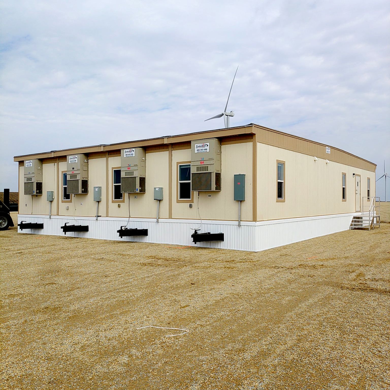 4-plex modular building with white skirting around the base of the mobile offices. HVAC units located on the end of each unit and a windfarm wind turbine located behind the office.